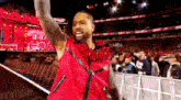 a man in a red vest is standing in front of a crowd at a wrestling match .