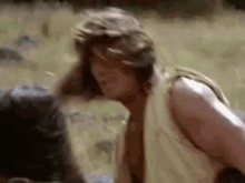 a man without a shirt is standing in a field with a backpack .
