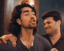 a man with long hair is making a funny face while another man holds his arm over his shoulder .