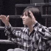 a young man wearing a plaid shirt is sitting down with his hands in his hair .