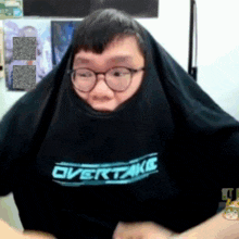 a man wearing glasses and a shirt that says overtake on it