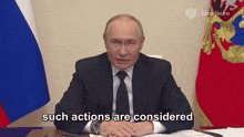 a man in a suit and tie says such actions are considered in front of a russian flag