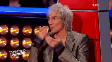 a man in a silver suit is sitting in a red chair with his hands in his pockets .