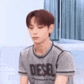 a young man wearing a diesel t-shirt is sitting on the floor .