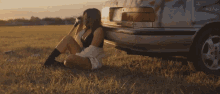 a woman is sitting in the grass next to a car with the license plate number lc