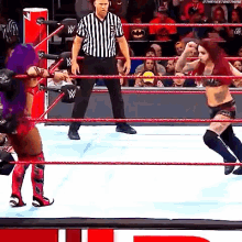 two women are wrestling in a wrestling ring while a referee stands in the corner .