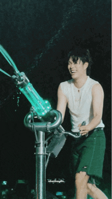 a man in a white tank top and green shorts is standing next to a machine that is spraying water