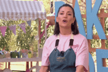 a woman wearing a pink shirt and an apron that says bake off on it