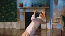 a woman in a white shirt is singing into a microphone in front of a fireplace