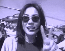 a woman wearing sunglasses is giving a peace sign in front of a helicopter