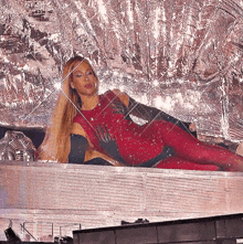 a woman in a red jumpsuit is laying on a stage