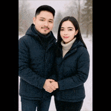 a man and a woman standing next to each other in the snow wearing blue jackets