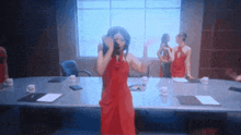a woman in a red dress stands at a conference table