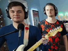 a man wearing headphones is playing a guitar next to another man