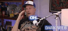 a man in a baseball cap is talking into a microphone while wearing a dark web shirt