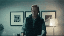 a man in a vest is standing in a room with a lamp