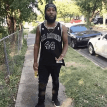 a man wearing a black san antonio jersey is standing on a sidewalk