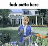 a woman in a blue jacket is standing in front of a house with the words fuck outta here below her