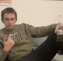 a man wearing a sweater that says son of a tv dad is holding a bottle of corona extra