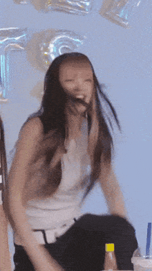 a woman in a white tank top is sitting in front of balloons that say t