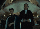 a woman in a cape stands next to a man in a suit