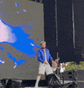 a man in a blue jacket and white shorts is dancing on a stage .