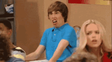 a boy in a blue shirt is making a funny face while sitting at a table with a group of people .