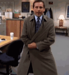 a man in a trench coat and tie is dancing in an office .