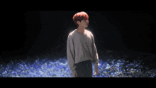 a young man with red hair is standing in a field of flowers