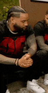 two men are sitting on a couch with their hands folded in prayer .
