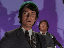 a man singing into a microphone with another man behind him