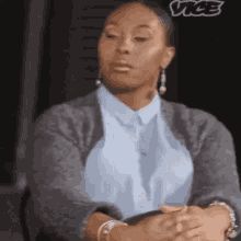 a woman is sitting at a table with her hands folded and looking at the camera .