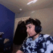 a man wearing headphones and a tie dye shirt is playing a video game in a room .
