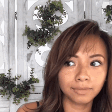 a close up of a woman 's face in front of a wall with plants on it
