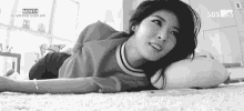 a black and white photo of a woman laying on her stomach on a carpet .