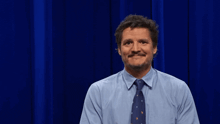 a man in a blue shirt and tie stands in front of a blue curtain that says thank you