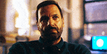 a man with a beard wearing a green shirt is sitting in a room