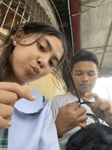 a girl is making a funny face while a boy is braiding his hair