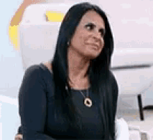 a woman with long black hair is sitting on a couch wearing a black dress and a necklace .