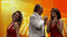 a man in a sequined suit is dancing with two women in red sequined dresses