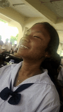 a girl wearing a white shirt with a black bow is smiling