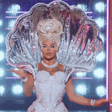 a woman in a white dress is wearing a silver shell shaped hat