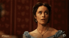 a woman is wearing a blue dress and a necklace and looking up .