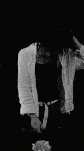 a black and white photo of a person in a white shirt looking at a flower .