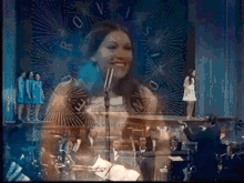 a woman singing into a microphone with a clock in the background that has the numbers 0 and 1