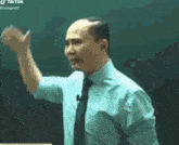 a man in a blue shirt and tie is giving a speech in front of a green board .