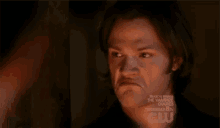 a man is making a funny face in a dark room with a cw logo behind him .
