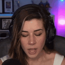 a woman wearing headphones and a white tank top is singing into a microphone .