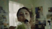 a woman is singing into a microphone in a room with her hair blowing in the wind .