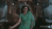 a woman in a green dress is dancing in a room in a video .
